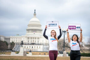 two women standing in front of national capitol holding voter signes